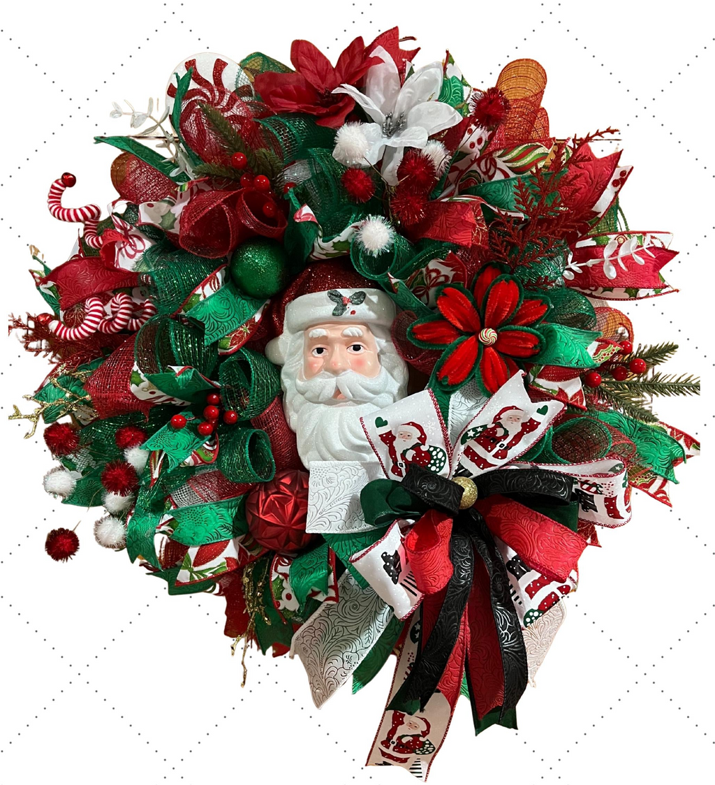 A festive Christmas wreath featuring a white Santa Claus face in the center, surrounded by red and green mesh ribbons, candy canes, pine branches, and decorative bows on a white background.