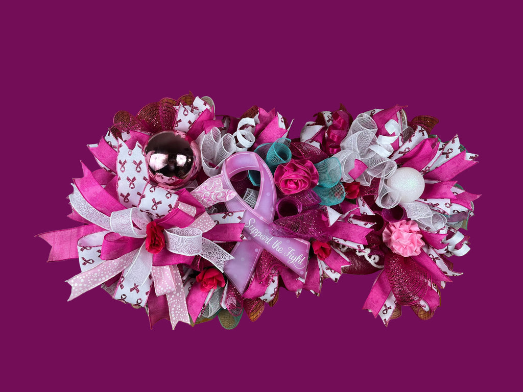 A festive pink and purple mesh doormat wreath with ribbons, bows, roses, and a metallic ball, hung on a brown wooden front door.