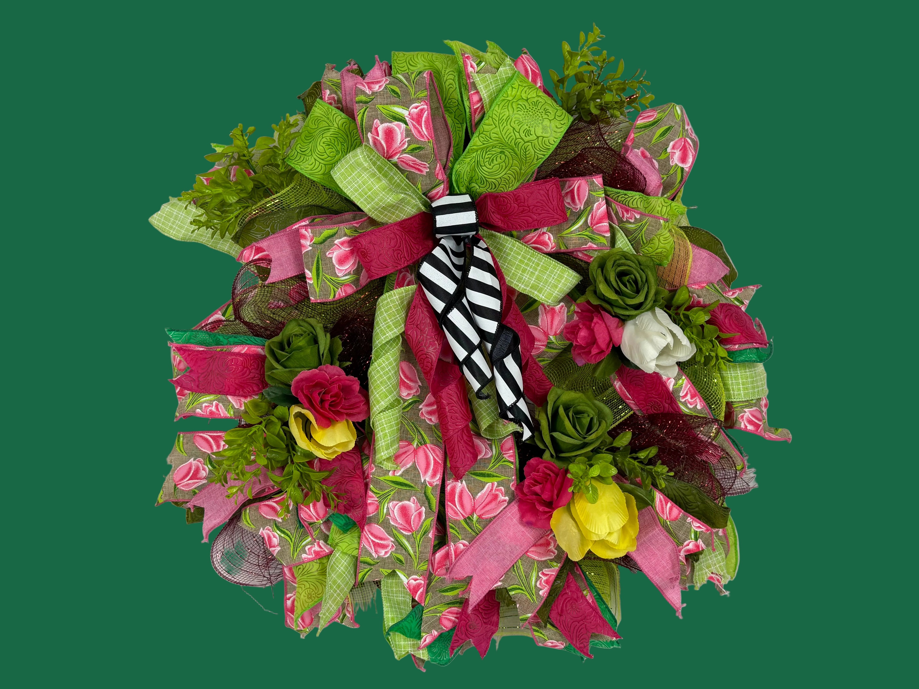 A decorative mesh wreath featuring pink and green floral patterns, green mesh ribbon, faux roses, and a black-and-white striped bow in the center, displayed against a plain white background.