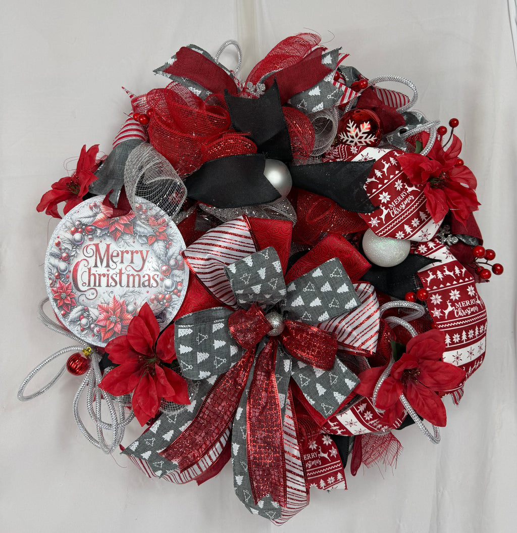 A festive Christmas wreath made of red, gray, and black mesh ribbons, decorated with red poinsettia flowers, silver ornaments, and a round hanging tag that reads 'Merry Christmas'.