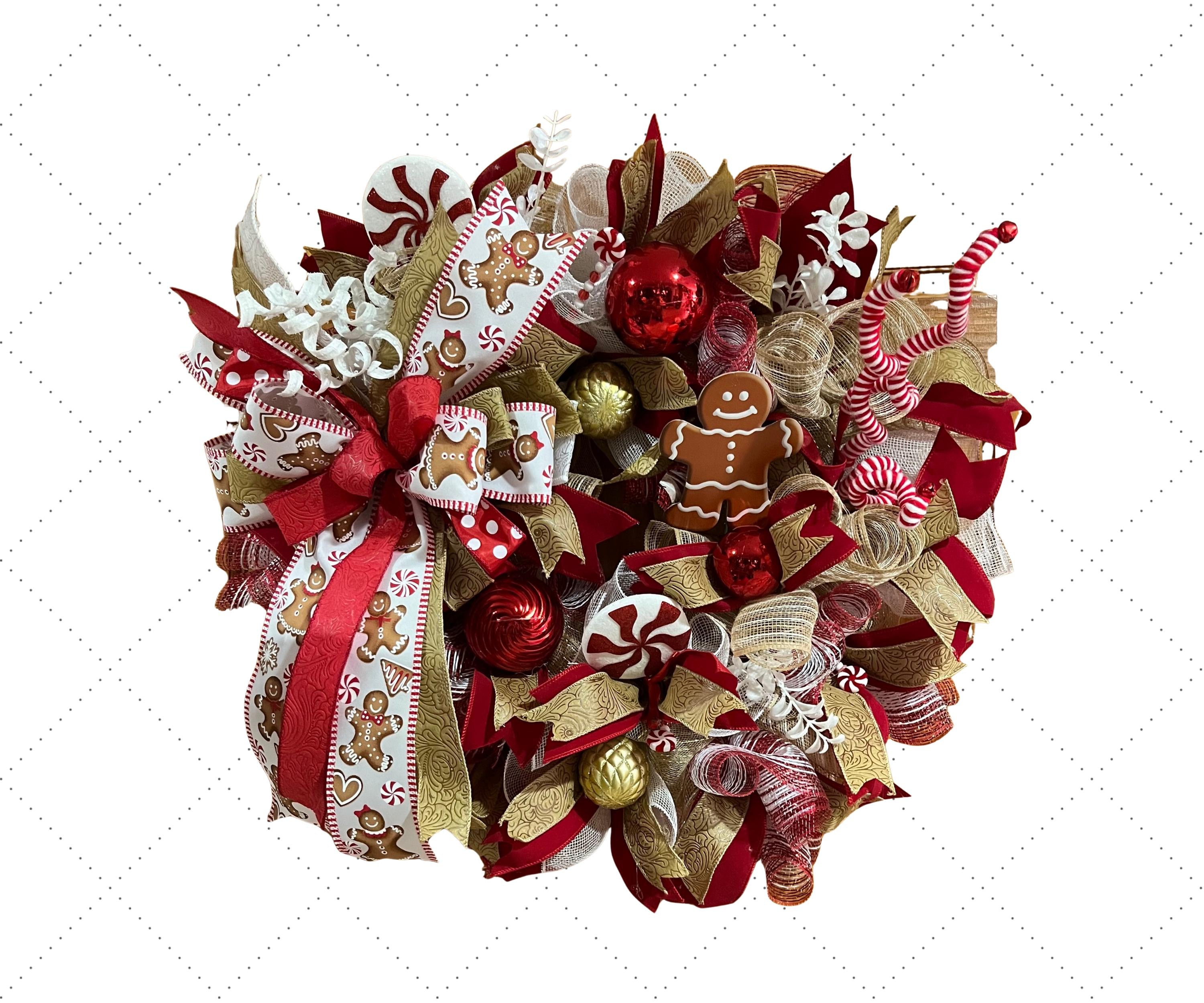 A festive Christmas wreath made of red and gold mesh ribbon with gingerbread cookies, candy canes, peppermint candies, and red ornaments, set against a white background with a faint grid pattern.